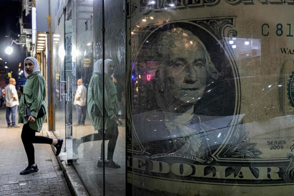 A woman walks out of a currency exchange shop displaying a giant US dollar banknote in the Zamalek ... [+]AFP VIA GETTY IMAGES